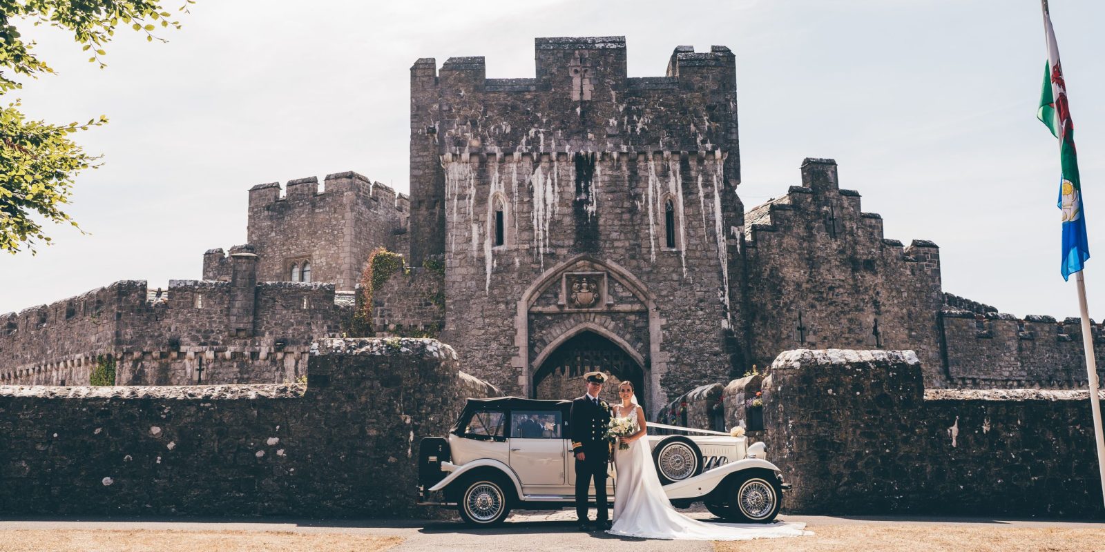 Bride and groom in front of St Donat's Castle entrance with wedding car and welsh and Scottish flag flying
