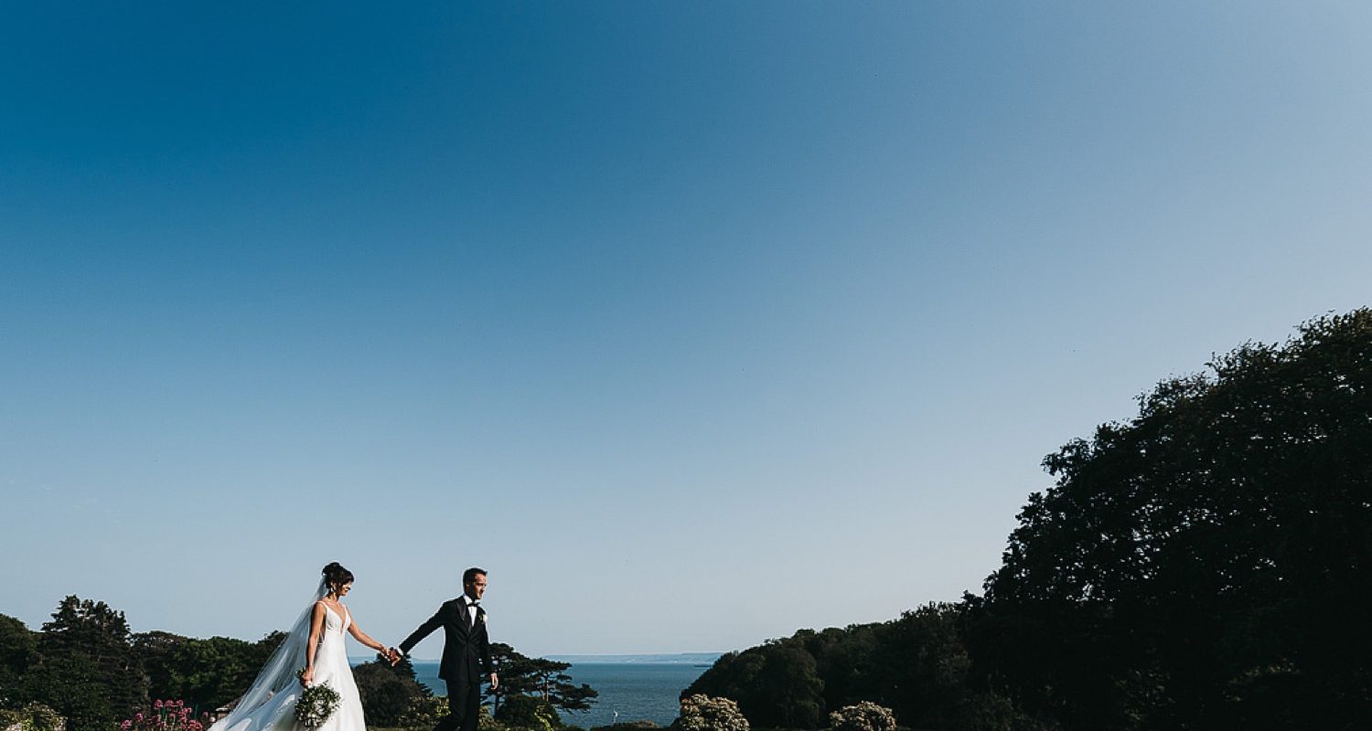 Bride and groom walking along top lawn with clear blue skies