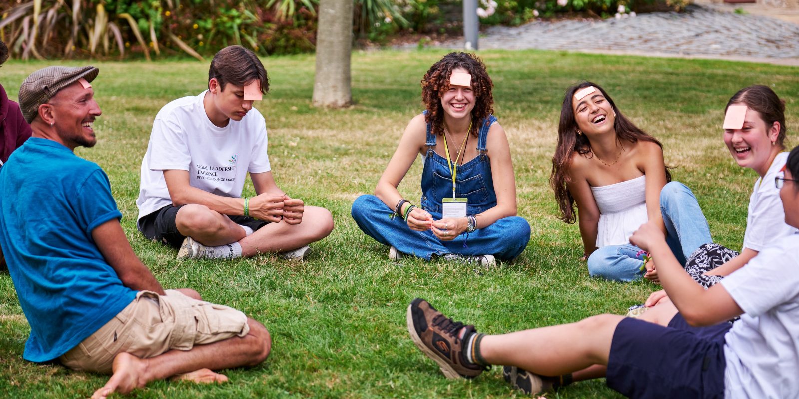 Group of GLE students sat on grass in a group discussing and playing a game